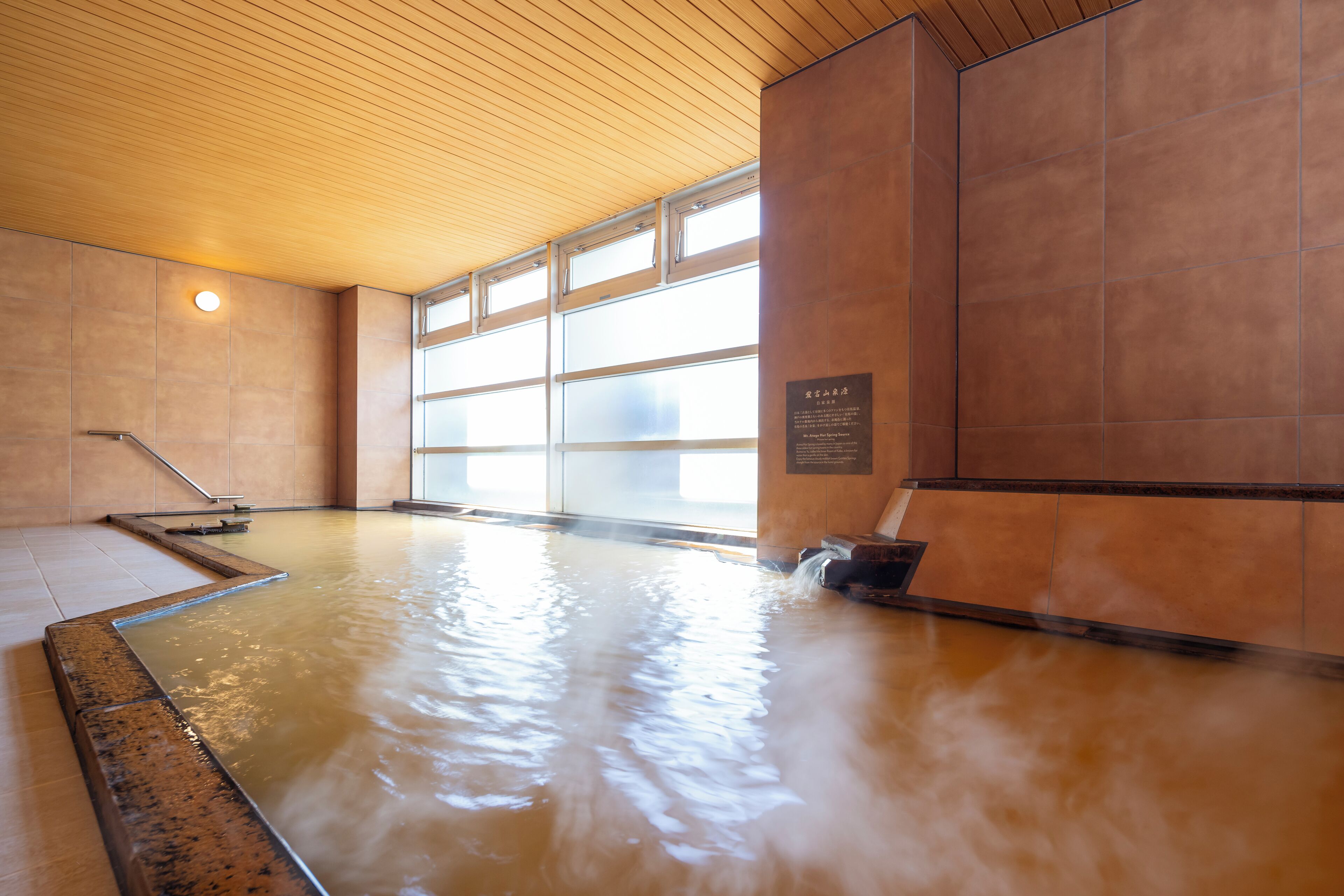 A hot tub area with tiled walls, a wooden ceiling, and a window providing natural light.