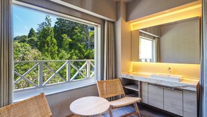 A balcony with wicker chairs, a round table, and a large window offering a view of greenery. - Kamenoi Hotel Arima (Kobe)