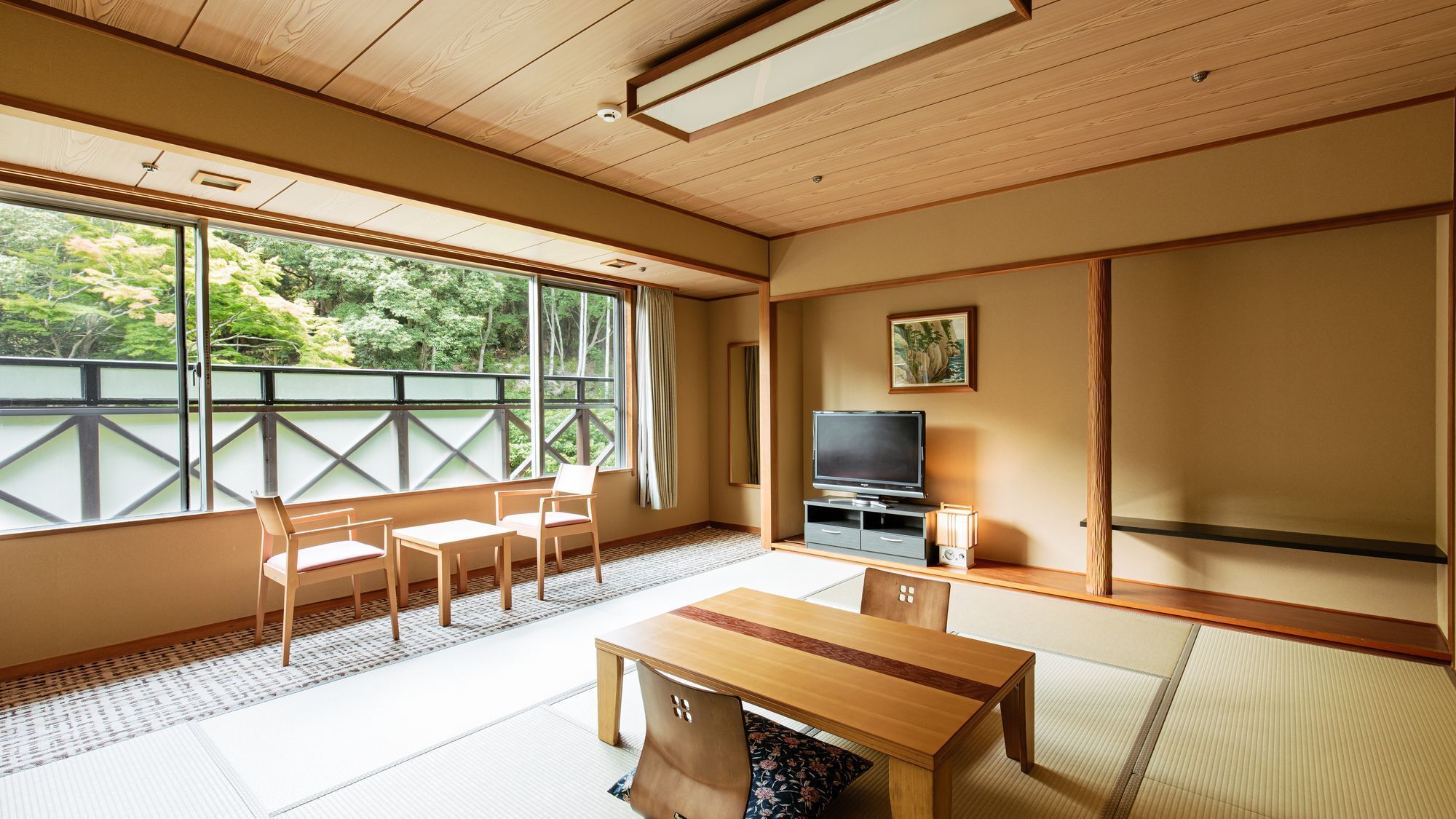 A traditional Japanese room with tatami flooring, a television, a table, and chairs.