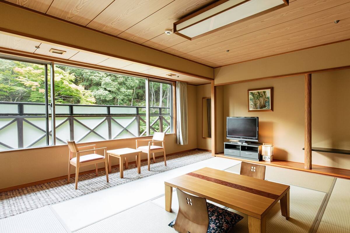 A traditional Japanese room with tatami flooring, a television, a table, and chairs.
