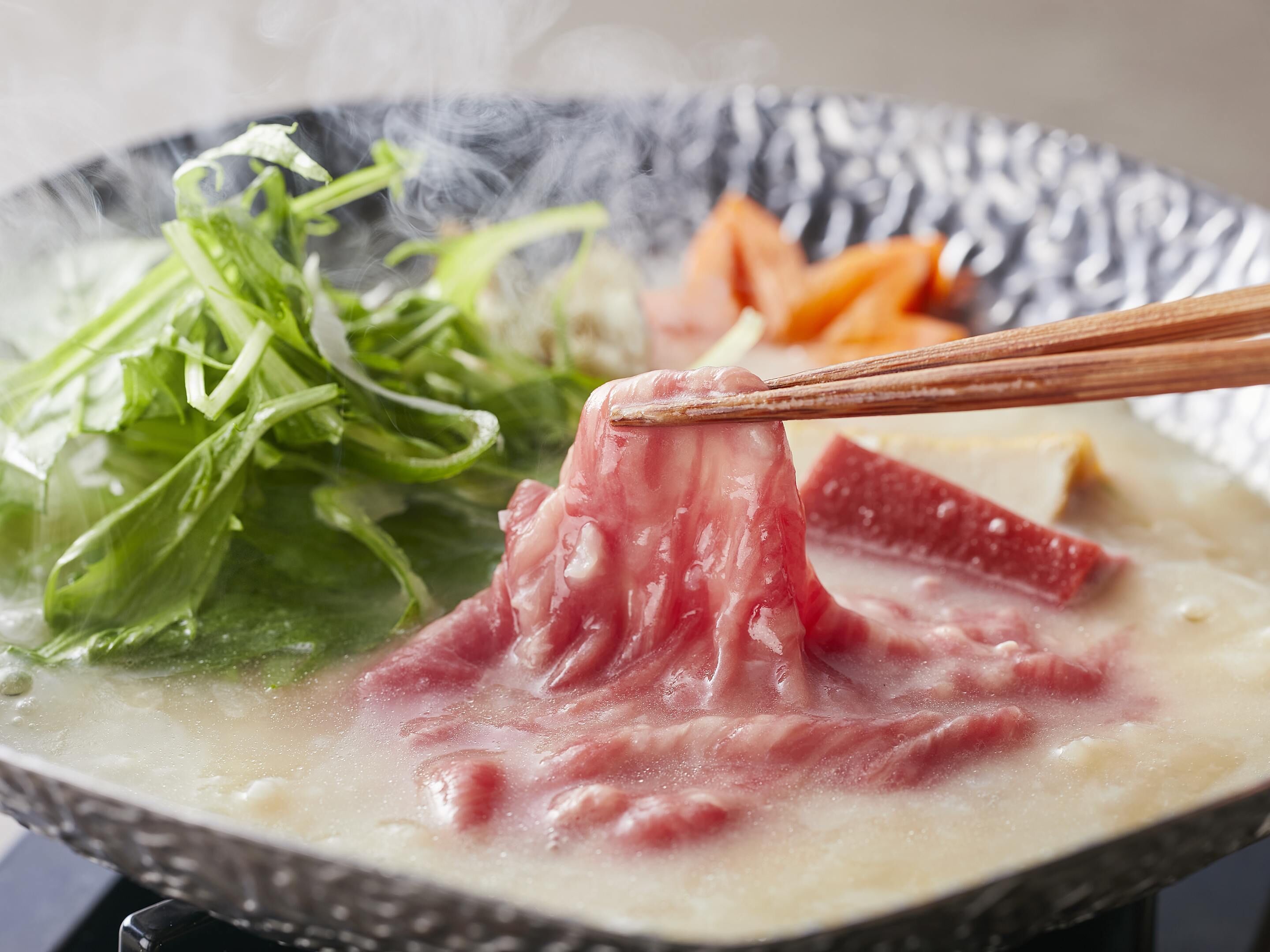 A bowl of hot broth with meat and vegetables.