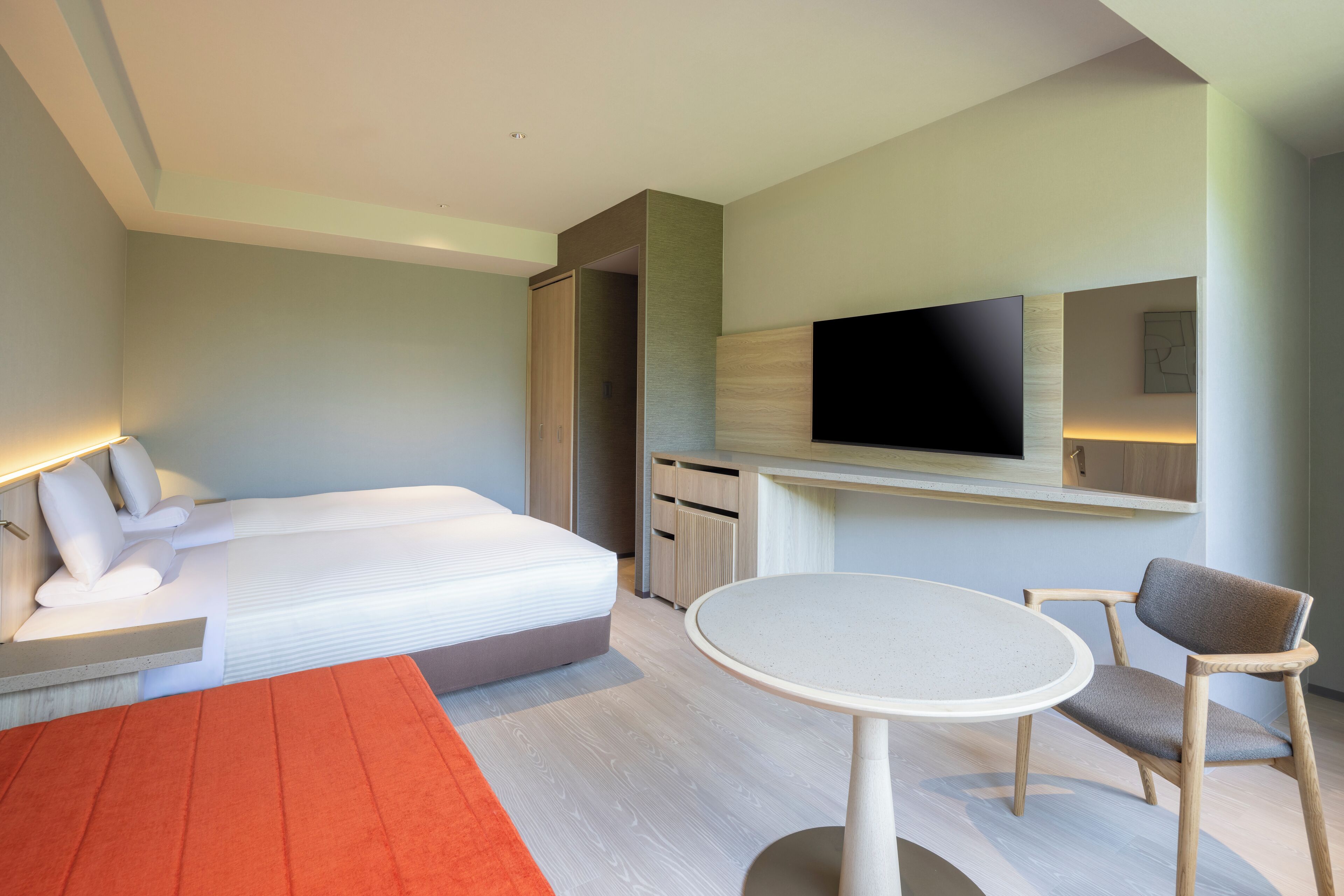 Una habitación de hotel moderna con una cama grande, una mesa redonda, una silla, un televisor y un armario.