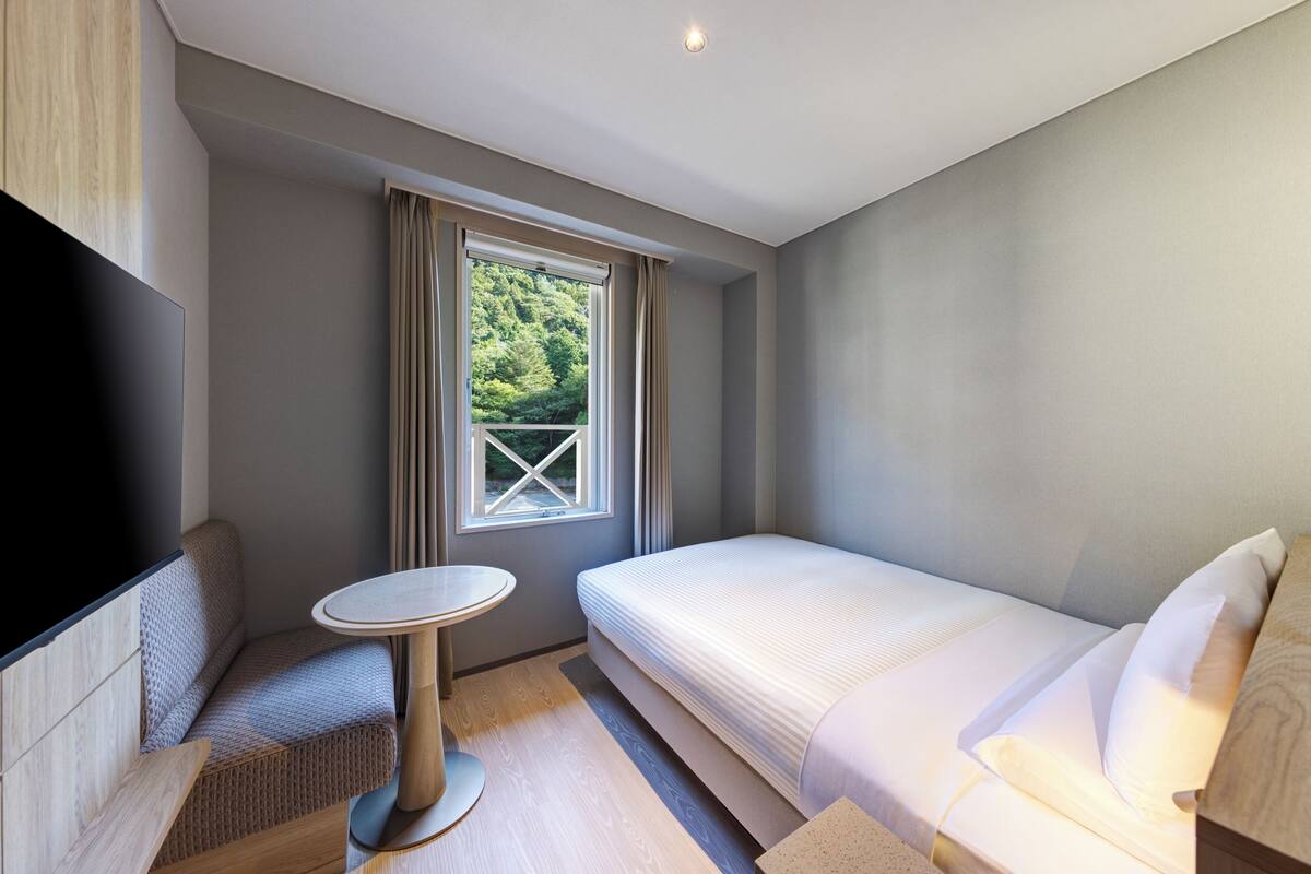 A modern hotel room with a bed, a small round table, a sofa, and a TV.