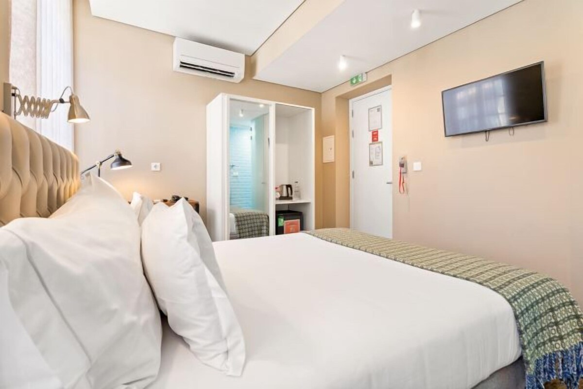 Een hotelkamer met een groot bed, een aan de muur bevestigde televisie, een airconditioning en een deur naar een badkamer.