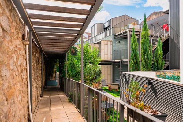 A narrow outdoor corridor with a pergola, stone walls, and a view of modern buildings. - Jardim da Batalha by Shiadu (Porto)