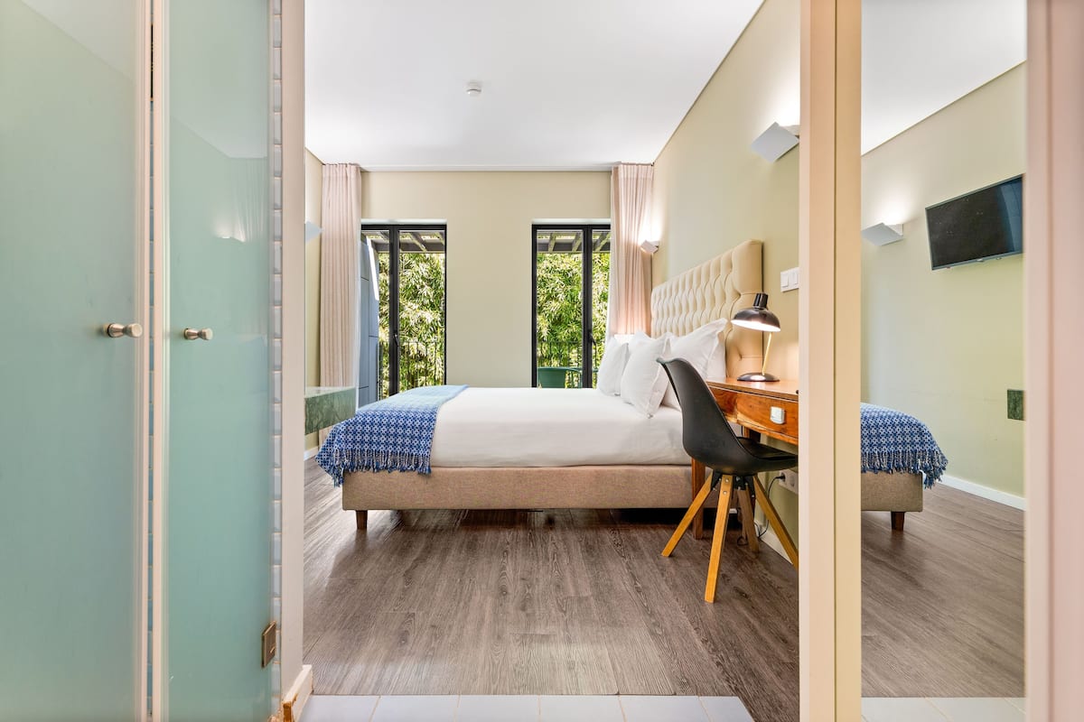 Ein modernes Schlafzimmer mit Bett, Schreibtisch und Stuhl, großen Fenstern und einem Flachbildfernseher.