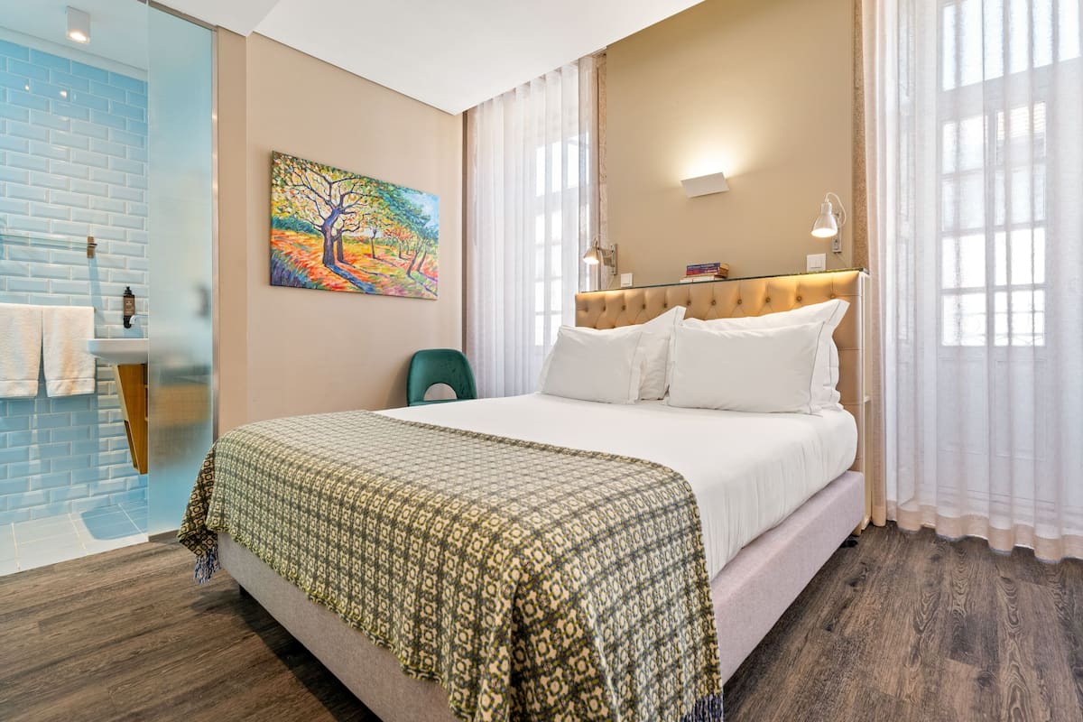 Ein Hotelzimmer mit Bett, einem Gemälde, einem Badezimmer mit blauen Fliesen und Holzboden.
