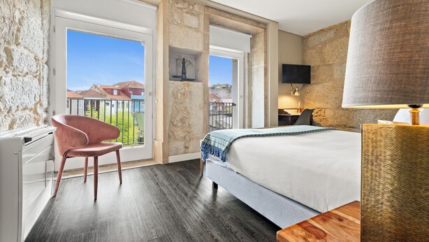 A hotel room with a bed, a chair, a desk, a TV, and a balcony with a view of buildings. - Jardim da Batalha by Shiadu (Porto)