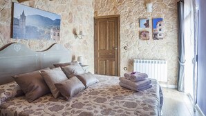 Ein Schlafzimmer mit einer Steinwand, einer Holztür, einem Bett mit floralem Bettzeug und einem Gemälde eines Schlosses.