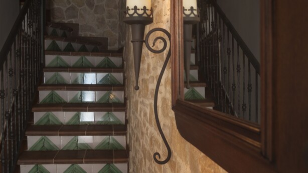Eine Treppe mit grün gefliesten Stufen, eine Steinwand und zwei Wandleuchter.