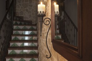 Una escalera con peldaños de azulejos verdes, una pared de piedra y dos velas fijadas a la pared.