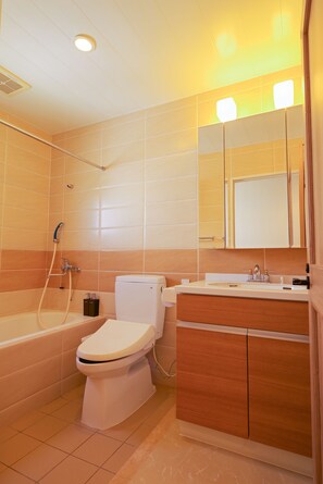A bathroom with a bathtub, toilet, and vanity with a mirror. - D and Stay Resort (Okinawa)