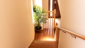 Un escalier en bois avec des rampes blanches, menant à un palier où se trouve un pot de fleurs.