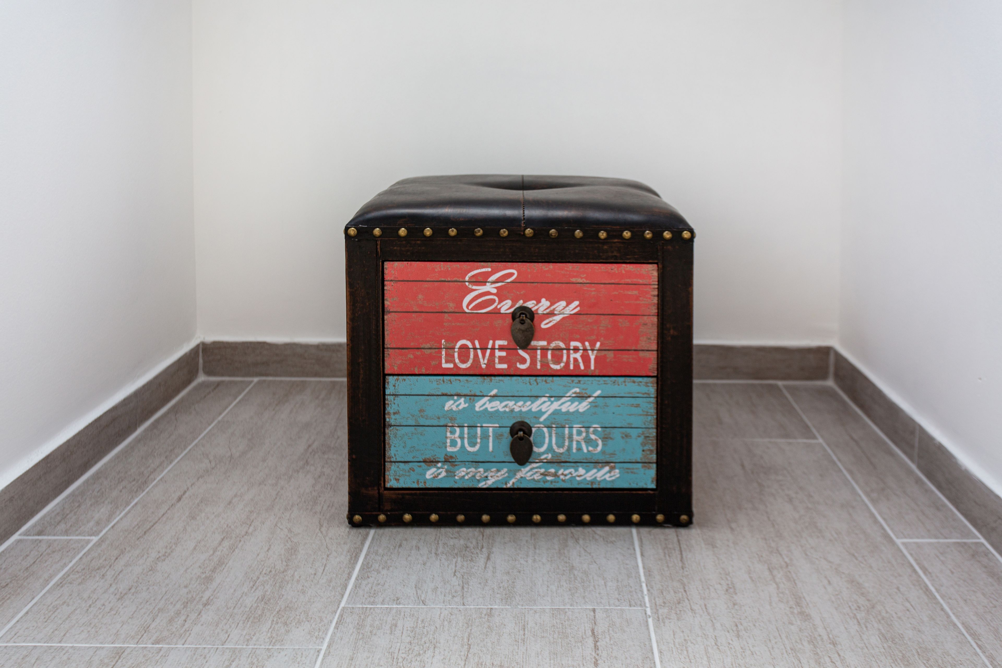 A small, square, wooden stool with a red, blue, and black color scheme and a sentimental message.