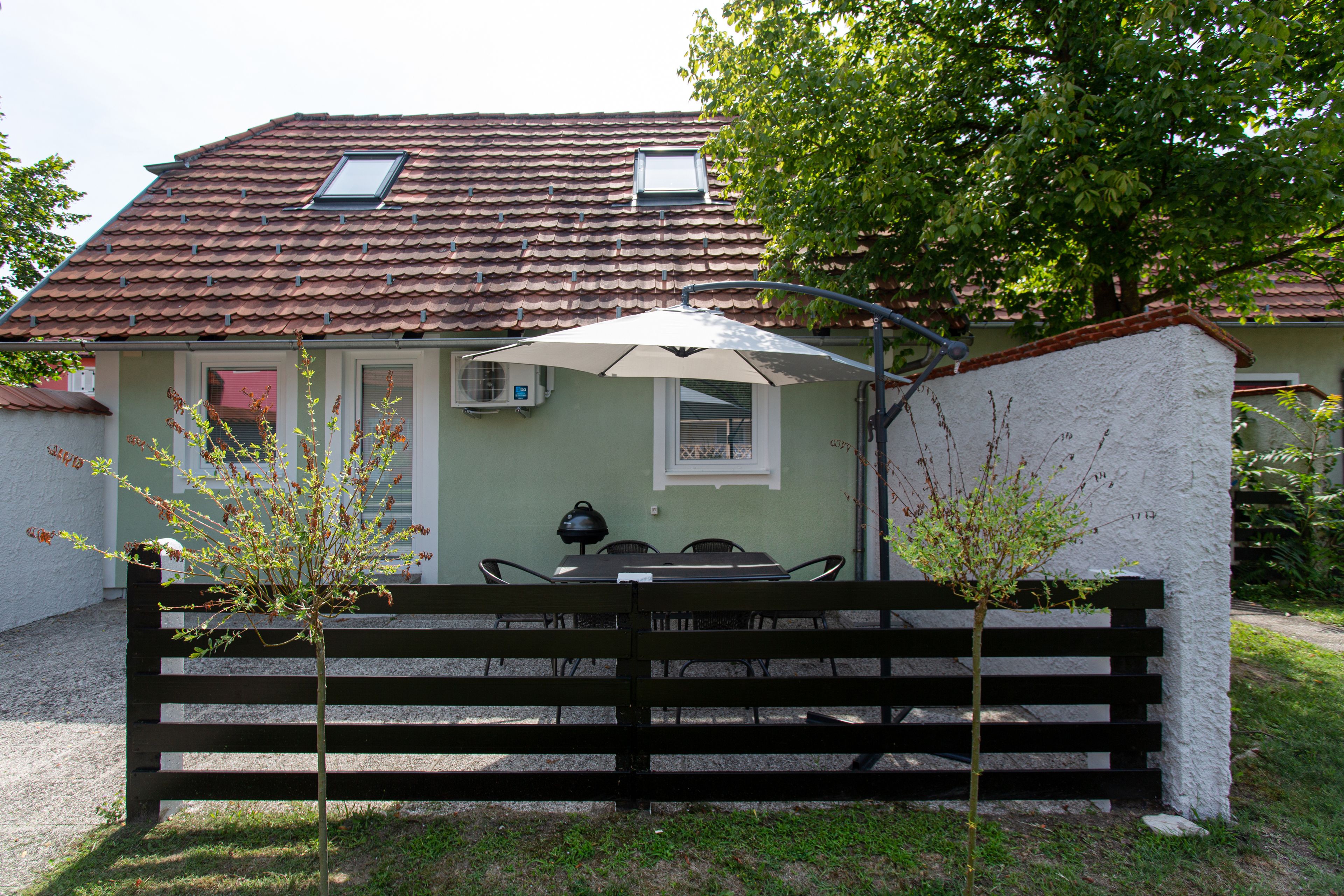 Une maison avec un toit en tuiles, un petit patio avec une table et des chaises, et un banc.