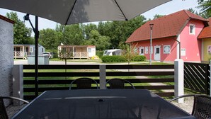 An outdoor patio with a table and chairs under a large umbrella, overlooking a residential area with houses and a parked car. - Holiday house in Terme Catez (Brezice)