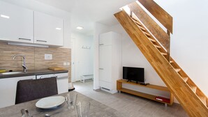 A modern kitchen with white cabinets, a wooden staircase, and a dining area with a table set for two. - Holiday house in Terme Catez (Brezice)