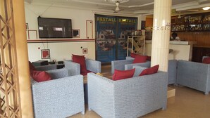 A hotel lobby with wicker sofas, a bar area, and a large poster advertising a guest lodge and pub. - Restall Guest Lodge (Adentan)