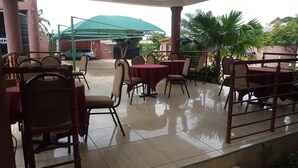 An outdoor seating area with tables and chairs, a green umbrella, and a car in the background. - Restall Guest Lodge (Adentan)