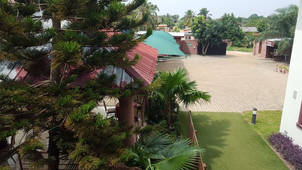 A courtyard with a paved area, surrounded by buildings and greenery, including trees and a lawn. - Restall Guest Lodge (Adentan)