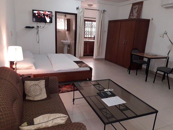 Habitación de hotel con una cama, una mesita de centro de vidrio, un sofá, un escritorio con una silla y un televisor en la pared.