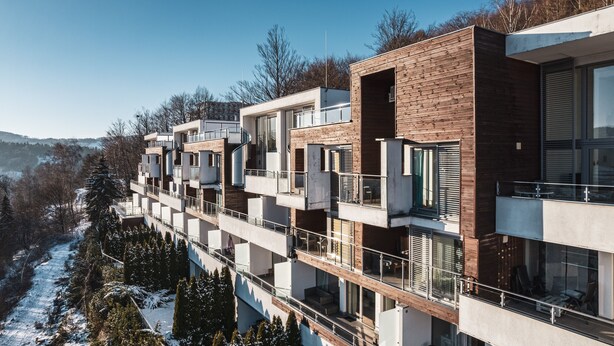 Ein modernes, mehrgeschossiges Wohngebäude mit Balkonen, großen Fenstern und einer verschneiten Landschaft im Hintergrund.