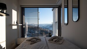 Ein Schlafzimmer mit großem Fenster, zwei Betten, einem Spiegel und einem Regal mit Gegenständen.