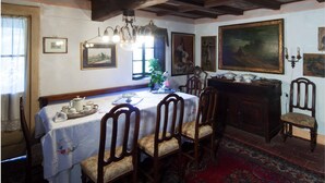 Een eetkamer met een houten tafel gedekt voor vier personen, omringd door stoelen. Daarboven hangt een kroonluchter en aan de muur een groot schilderij.