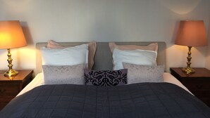 Una cama con colcha oscura, dos mesitas de noche con lámparas y almohadas estampadas.