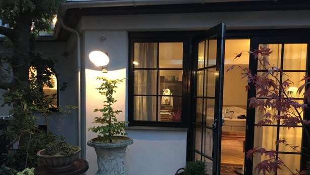 Una entrada tradicional al estilo japonés con una puerta de madera, un farol de piedra y plantas en macetas.
