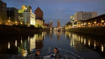 A boat on a river with buildings on the opposite bank.