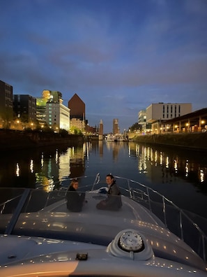 A boat on a river with buildings on the opposite bank.
