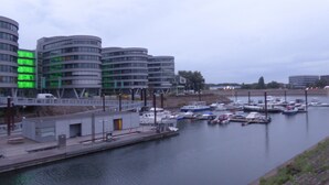 A marina with several boats docked, surrounded by modern buildings with curved architecture. - Rhein Yacht Lexa (Duisburg)