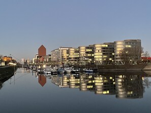 A waterfront cityscape with modern buildings, a calm river, and boats docked along the shore. - Rhein Yacht Lexa (Duisburg)