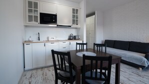 A compact kitchen with white cabinetry, a microwave, and a toaster. There is a dining table with chairs and a sofa in the adjacent living area. - Apartamenty Sun & Snow Kamienna (Wisla)