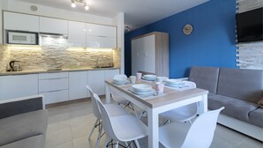 A modern kitchen with white cabinets, a stone backsplash, and a dining area with white chairs and a table set for four. - Apartamenty Sun & Snow Kamienna (Wisla)