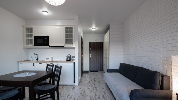 A compact living space with a kitchenette, a dining table with chairs, a sofa, and a white brick wall. - Apartamenty Sun & Snow Kamienna (Wisla)
