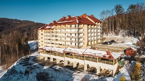 A multi-story hotel with balconies, a covered parking area, and a view of a snowy landscape. - Apartamenty Sun & Snow Kamienna (Wisla)