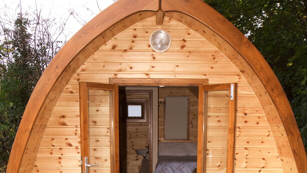 Una estructura de madera en arco con una puerta que da a un dormitorio con cama y ventana.
