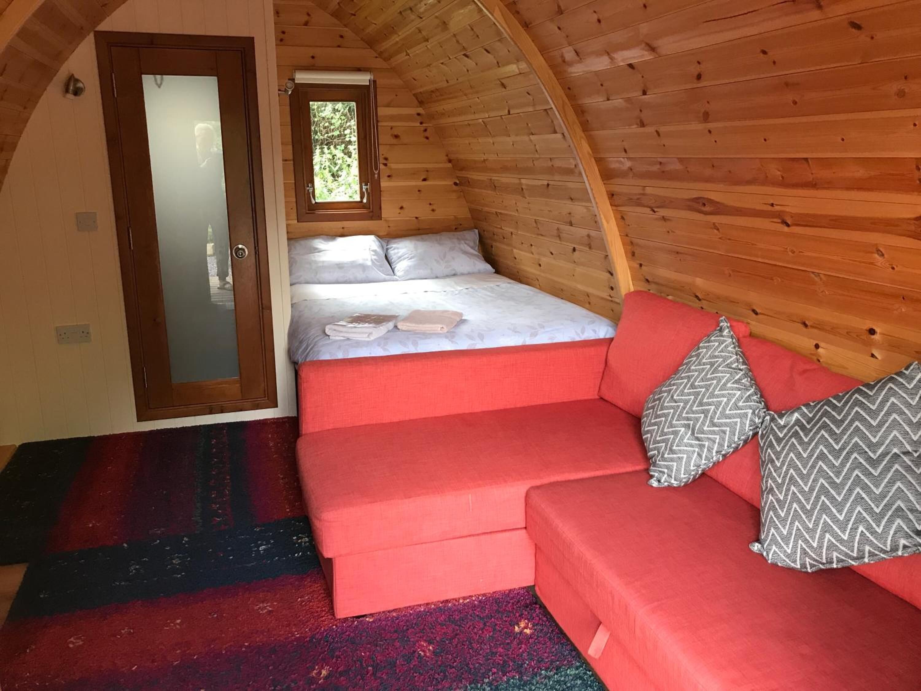 Una habitación acogedora con una cama, un sofá rojo y un ventanal pequeño.
