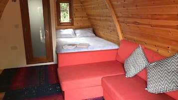 Una habitación acogedora con una cama, un sofá rojo y un ventanal pequeño.