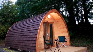 Una pequeña estructura de madera semicircular con una puerta y dos sillas afuera.