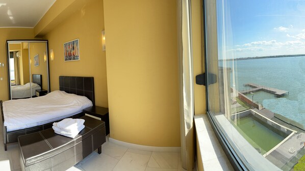 A hotel room with a bed, bedside table, and a large window offering a view of a dock and water. - Apart holiday Sophia Mamaia (Constanta)