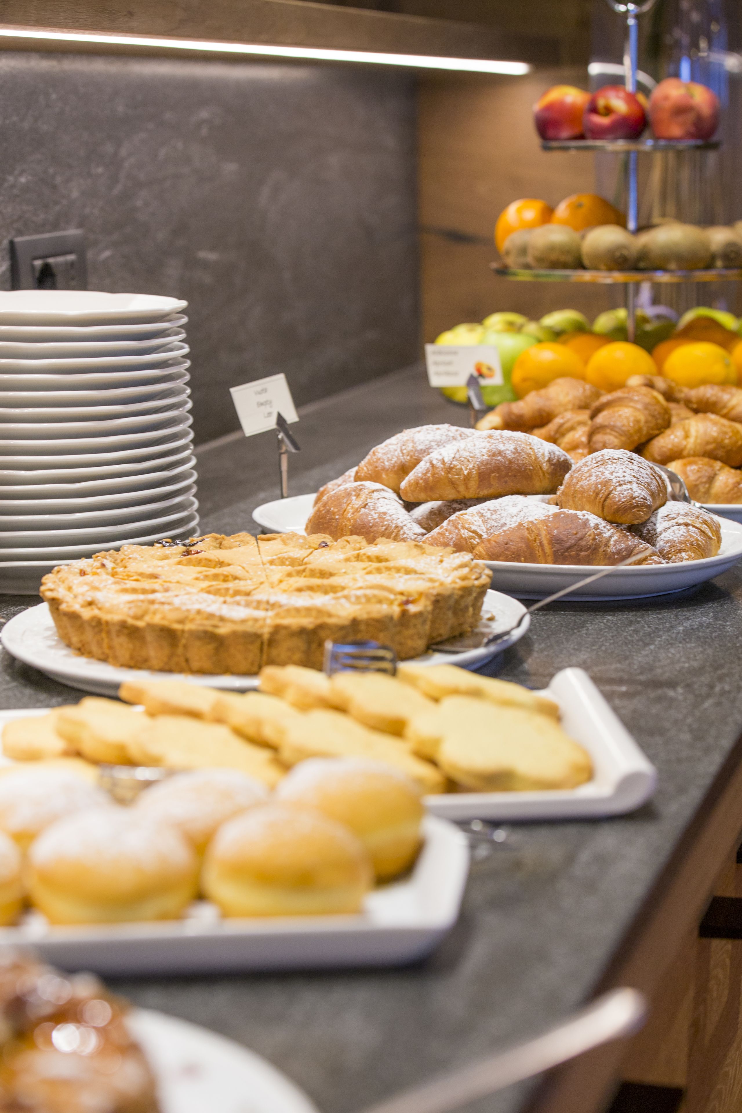 Un bufé con diversos pasteles, frutas y una pila de platos.