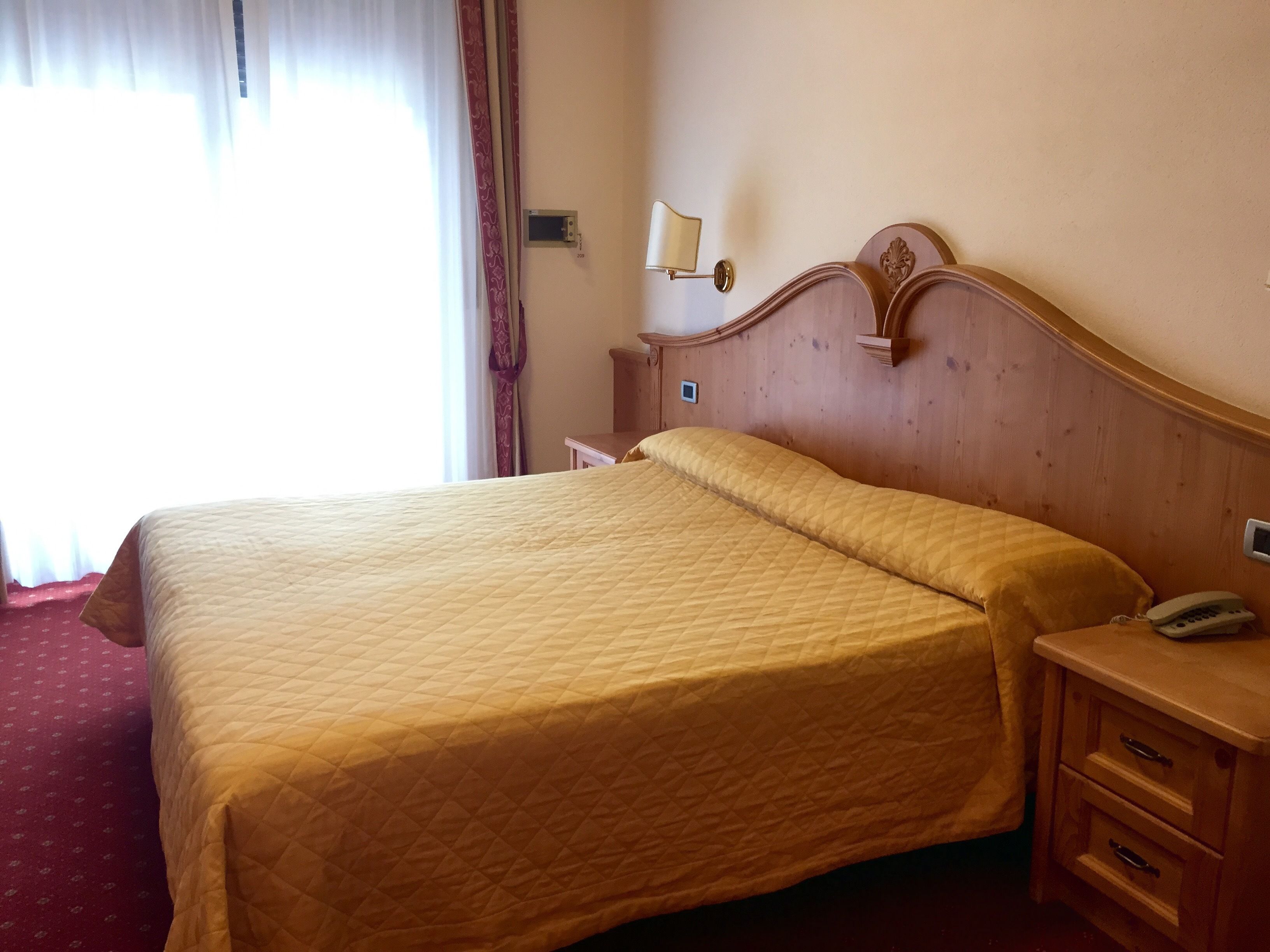 A hotel room with a large bed, wooden headboard, bedside tables, a lamp, and a telephone.