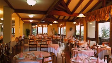 Un restaurante con varias mesas redondas cubiertas con manteles blancos y servilletas rosas, sillas de madera y un techo alto con vigas a la vista.