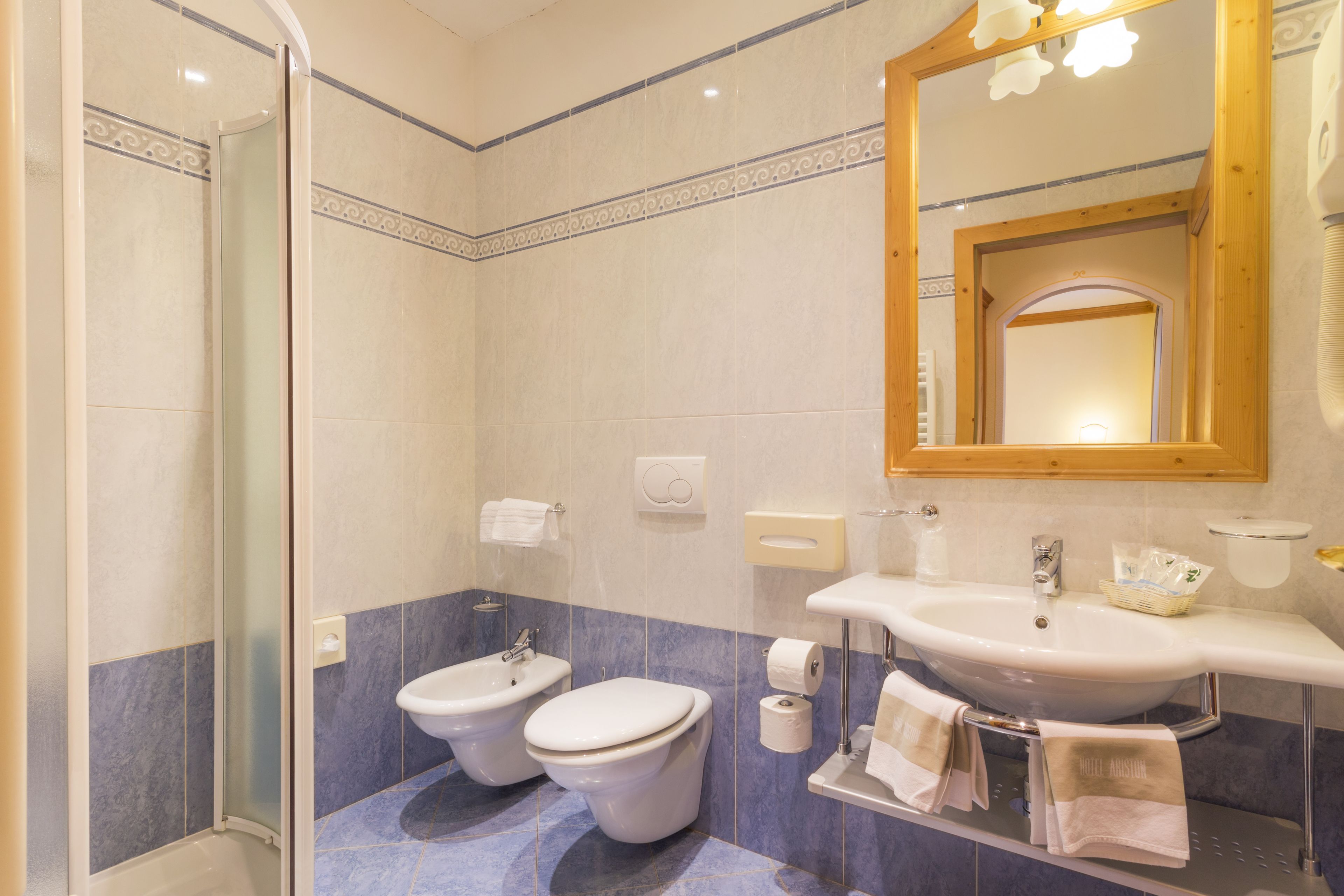 A bathroom with a glass shower enclosure, two toilets, a sink, and a mirror.