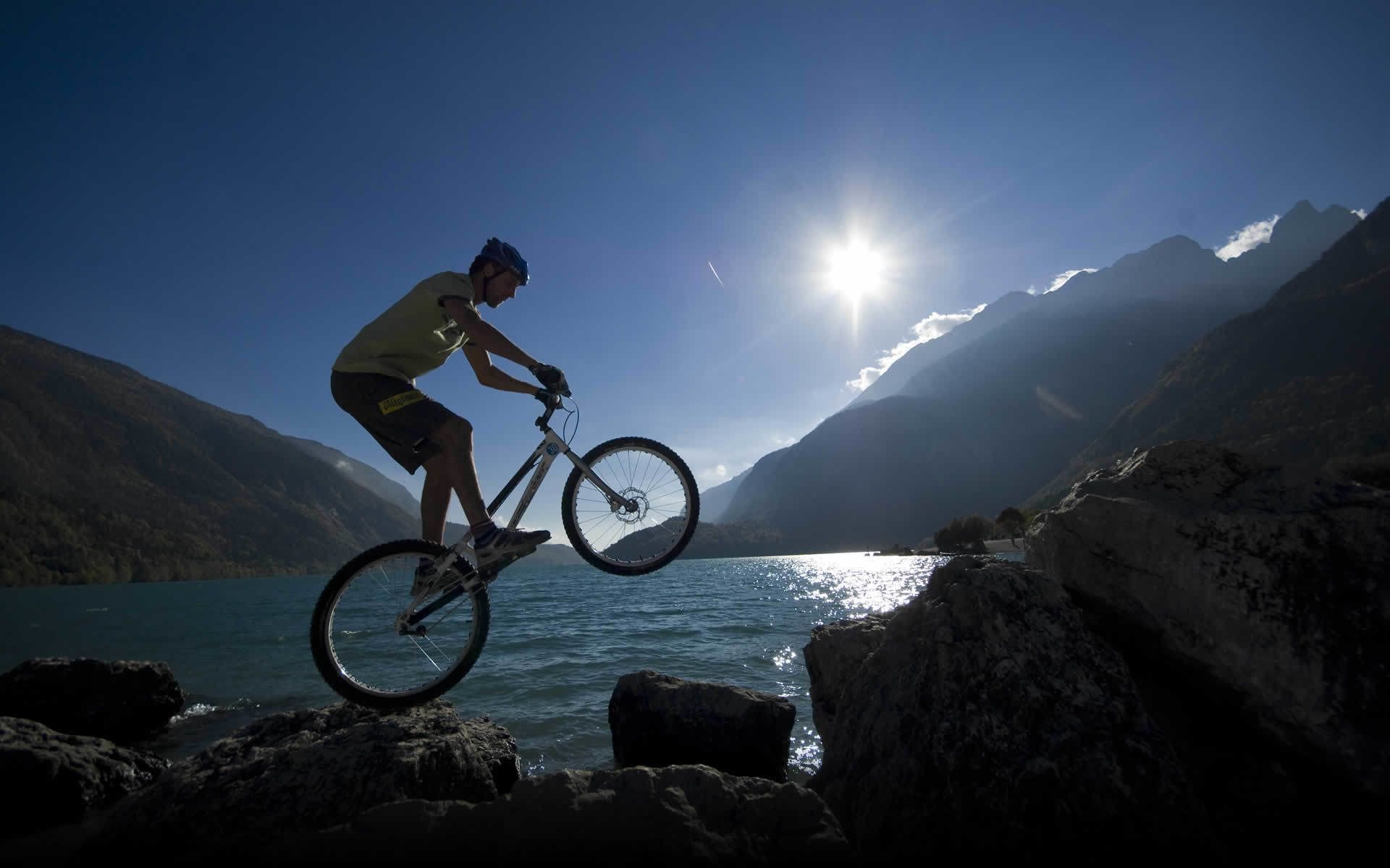 A mountain biker performing a jump over rocks with a lake and mountains in the background.