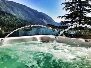 Un jacuzzi con vista a la montaña, rodeado de exuberante vegetación y cielo despejado.