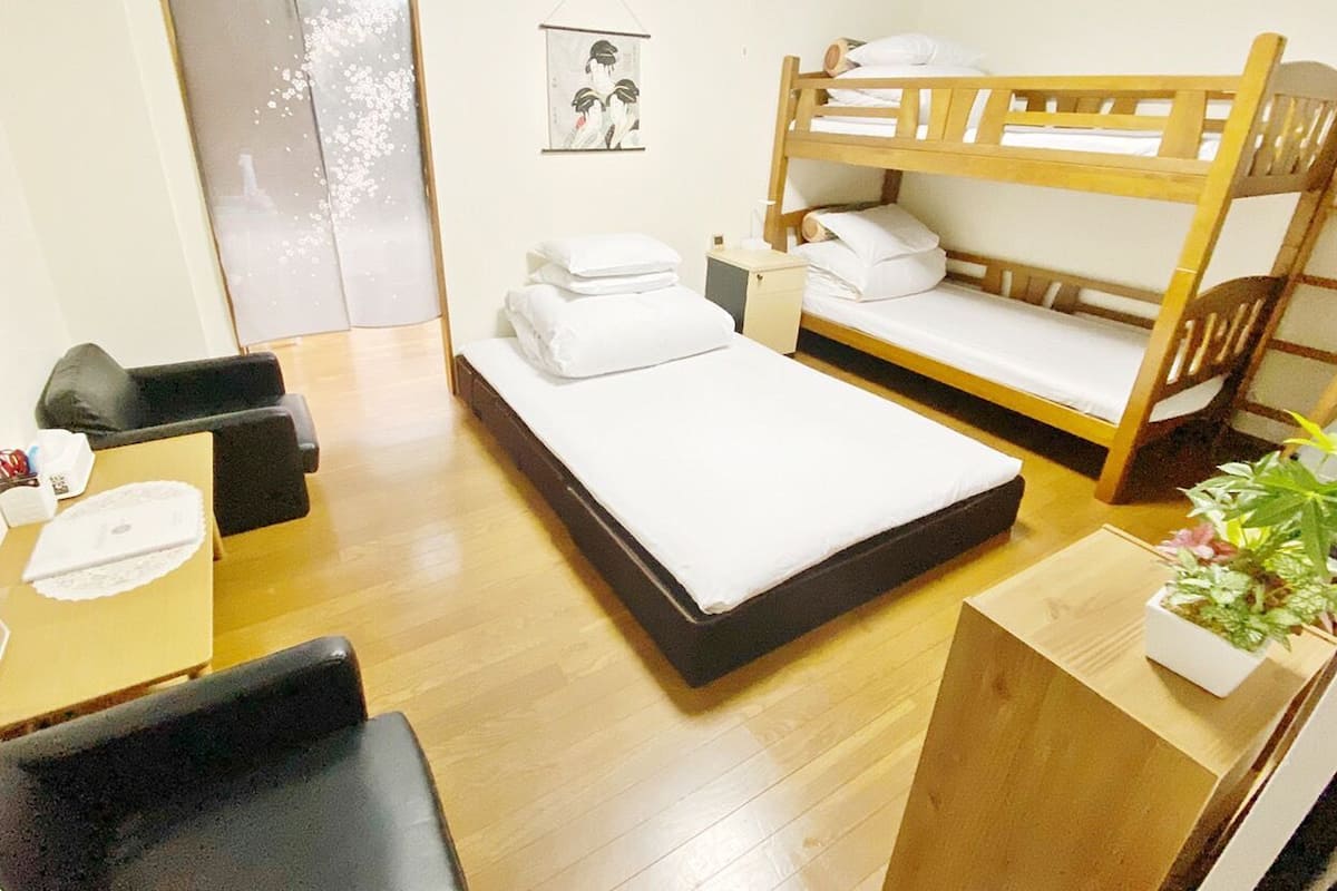 A room with a bunk bed, a desk with a chair, a small table, and a potted plant.